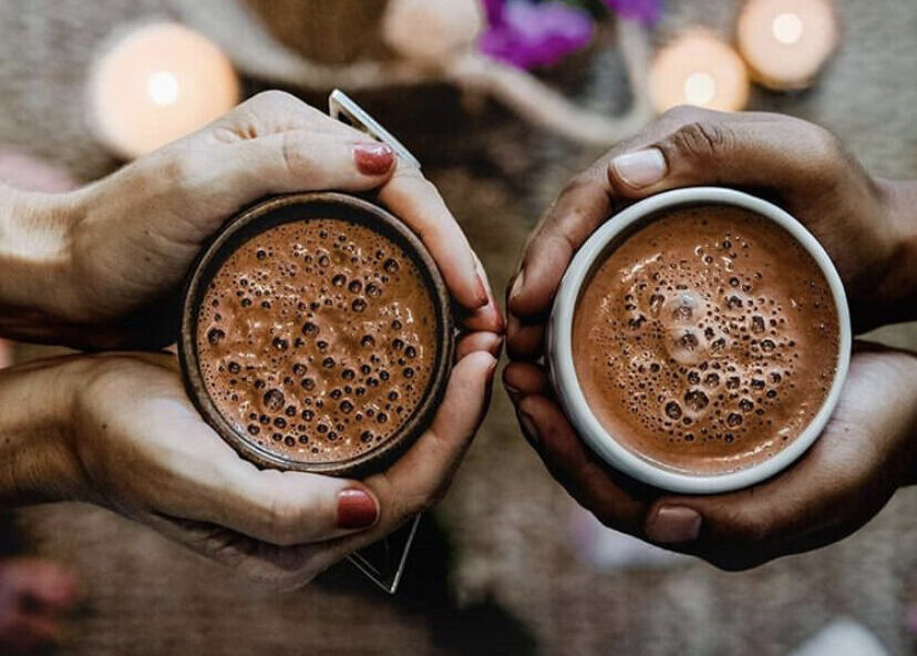 two pair of hands holding cups of cacao